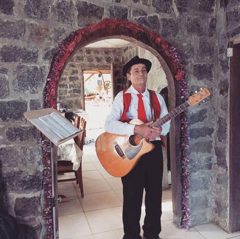 Dionísio com violão dentro de casa de pedra que construiu praticamente sozinho 