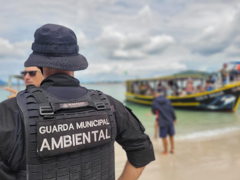 Foto mostra guarda municipal ambiental de costas diante da praia Ilha do Campeche com embarcação irregular na frente