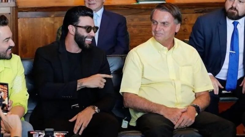 Gusttavo Lima sentado ao lado de Bolsonaro sorrindo