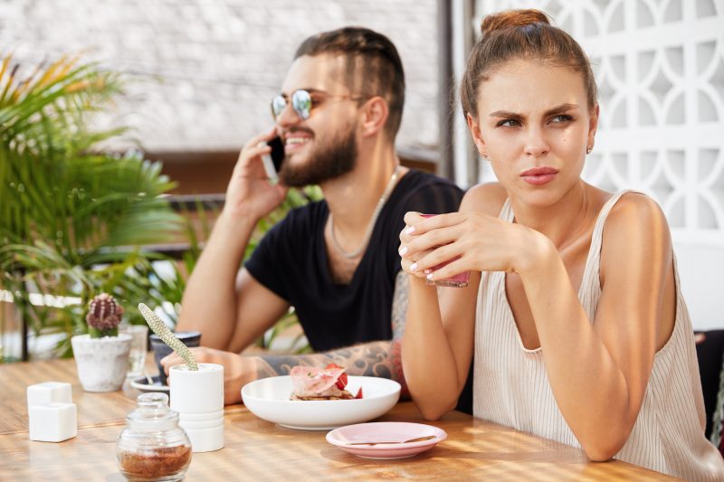 Homem falando ao telefone e mulher olhando para o lado oposto com uma expressão de desconforto 