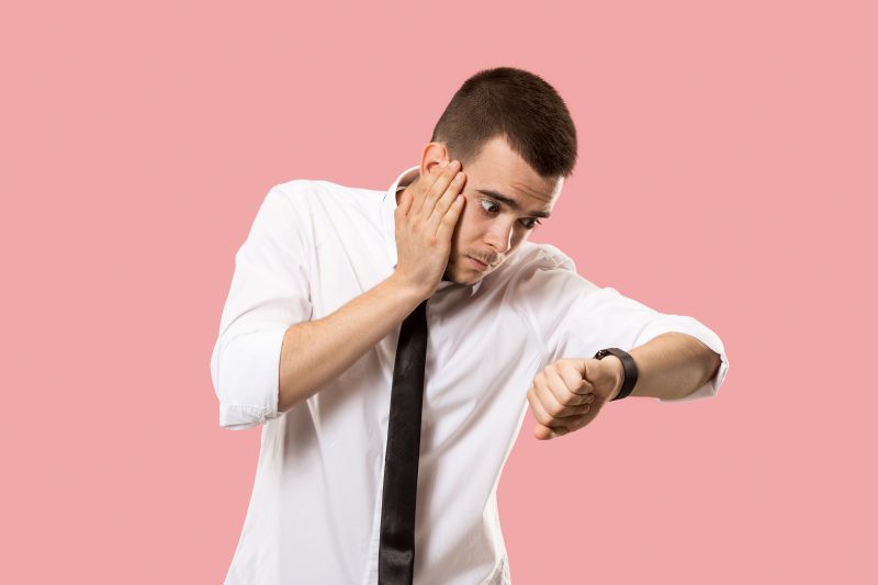 na foto homem olha perplexo para relógio como uma pessoa está sempre atrasada