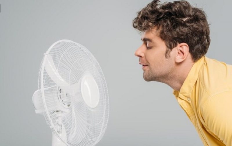 na foto aparece um homem que tenta esfriar a casa com um ventilador