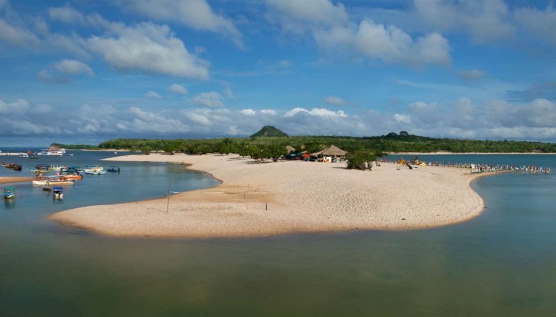 Imagem de uma faixa de areia circundada pela água com barcos ao redor 