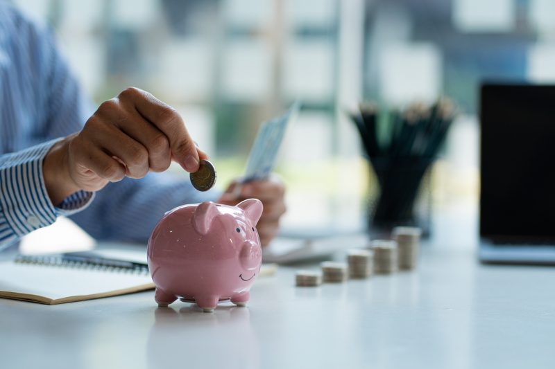 mãos de um homem colocando moedas em cofrinho e segurando dinheiro para economizar despesas