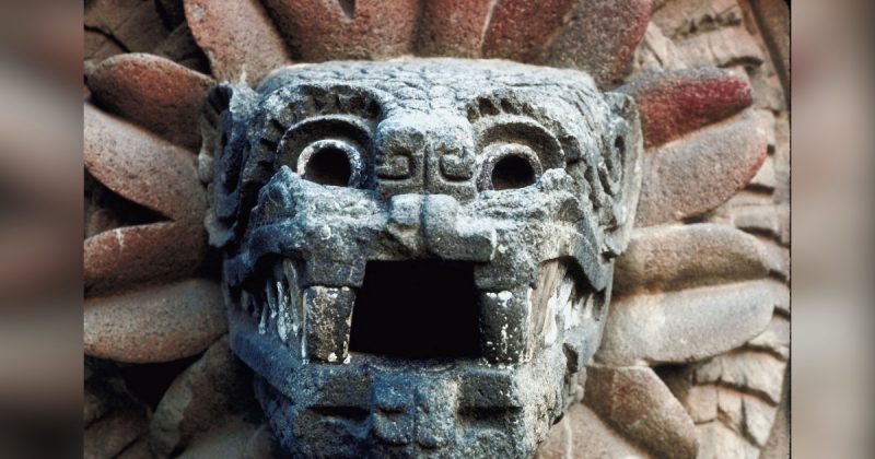 Escultura maia de monstro de pedra por trás umas flores