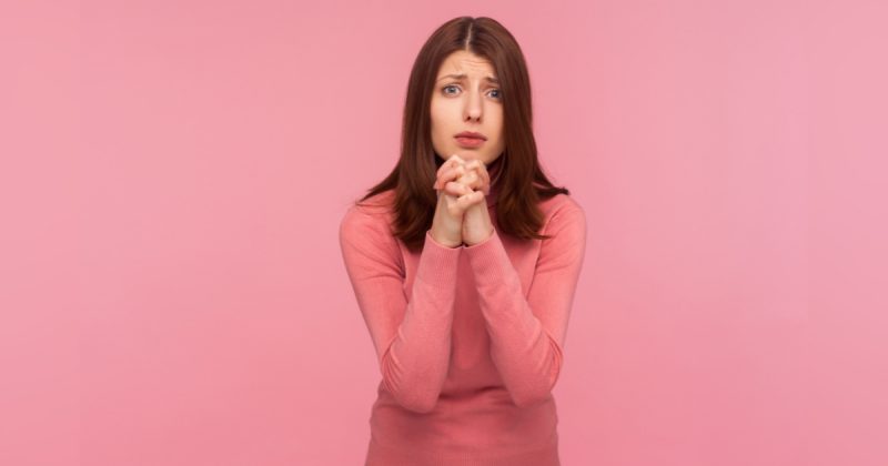 Mulher vestida de rosa com as mãos juntas e rosto apreensivo