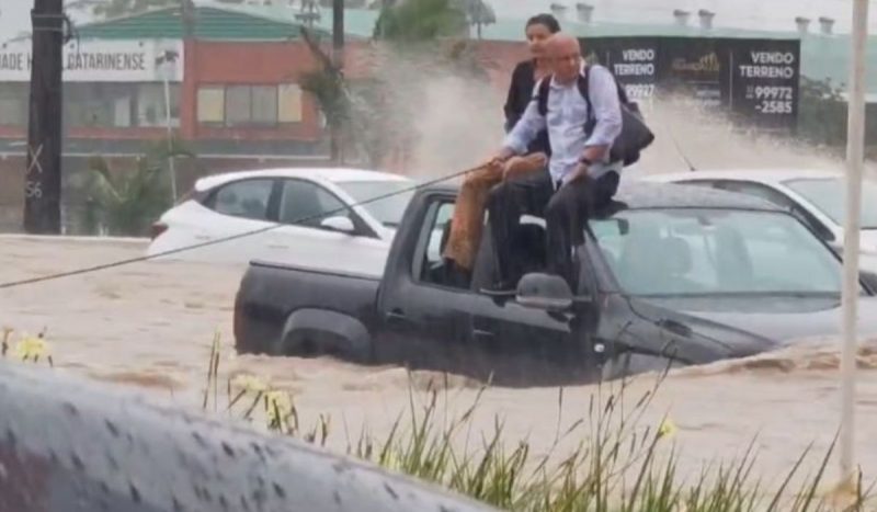 Casal sentado no teto de um carro em meio à chuva em Florianópolis