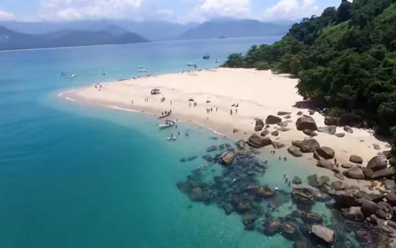 Praia com água azul cristalina, pedras e areia clarinha 