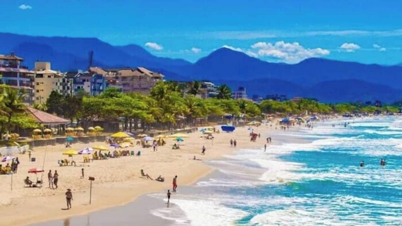 Foto de uma praia com pessoas na areia e prédios ao fundo 