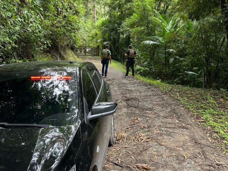 A imagem mostra um carro e policiais em frente ao corpo do maior sequestrador e assaltante de Santa Catarina 