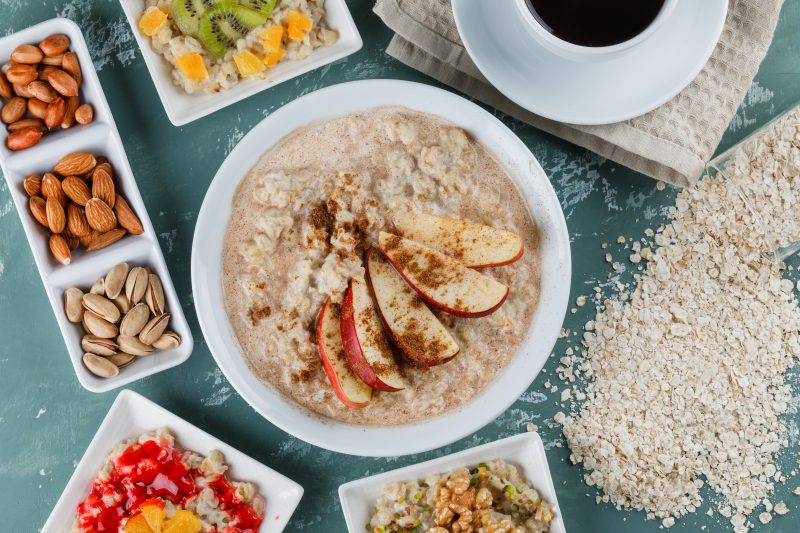 Aveia em pratos com frutas, geleia, nozes, canela, café e flocos de aveia dispostos sobre um fundo de gesso em vista plana.