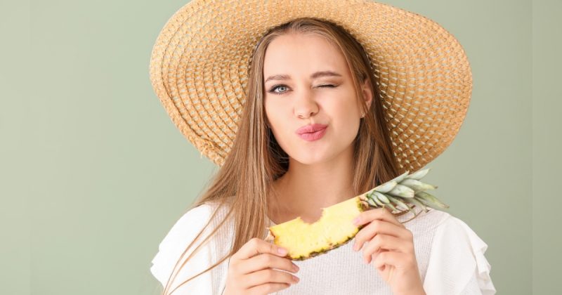 Mulher com abacaxi na mão fazendo um biquinho e sorrindo