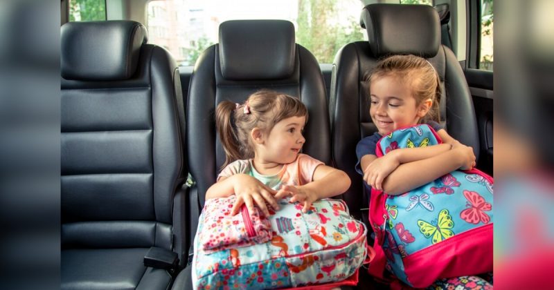 Duas crianças sentadas em baco de carro segurando bolsas coloridas