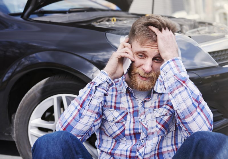 homem sentado em frente a carro estragado com a mão na cabeça representando 5 coisas no seu carro que bloqueiam a riqueza e a prosperidade