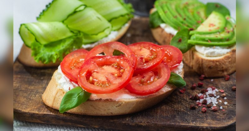 Rodelas de abacate com tomate em cima de tabua marrom