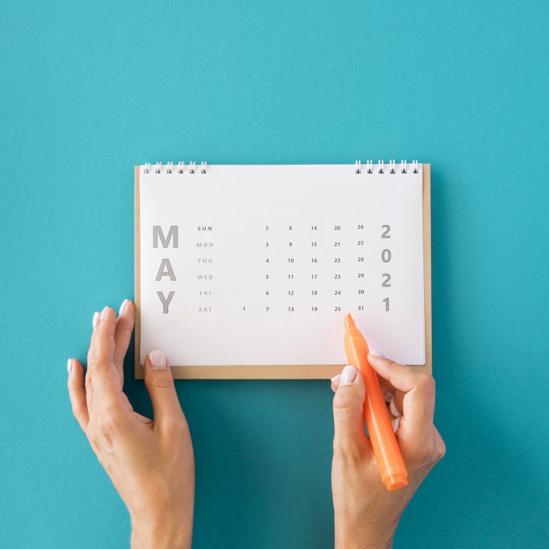 Mãos de uma mulher segurando uma canetinha de cor laranja marcando um dia e mês da sorte no calendário