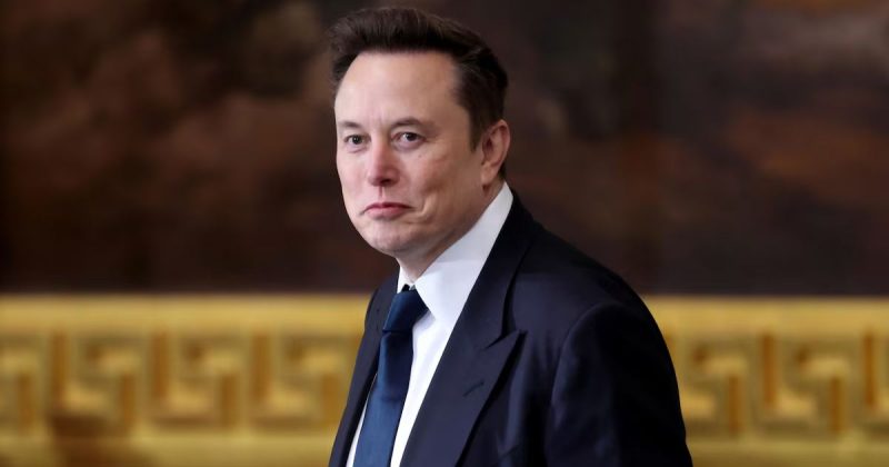 Elon Musk, homem branco, com terno e gravata, visto de perfil