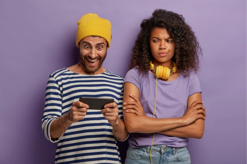 homem jogando no celular e a mulher ao lado esta irritada 