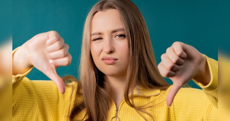 Mulher de camisa amarela com polegares para baixo