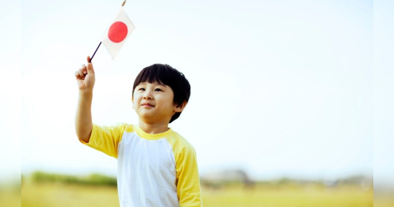 Menino japonês com bandeira do Japão nas mãos em meio ambiente