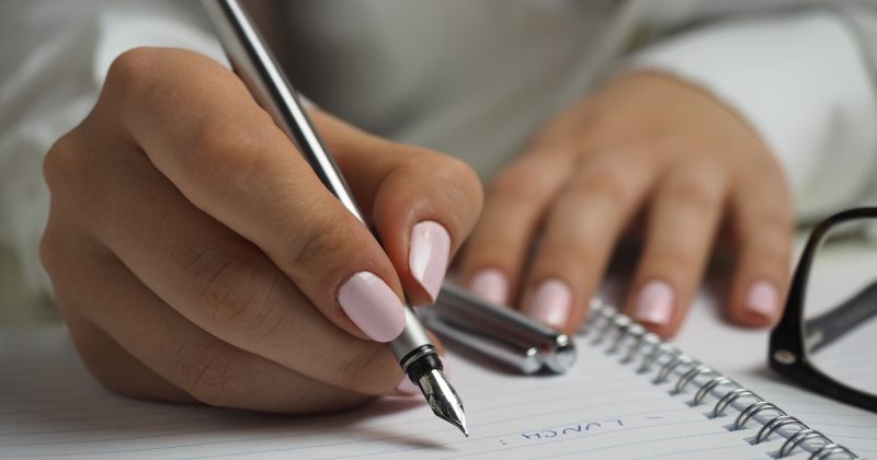 Mulher escrevendo em caderno com caneta prateada