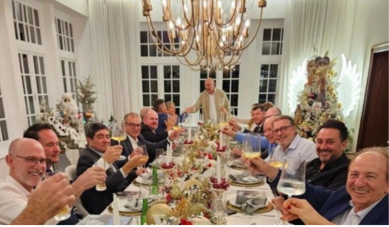 Jantar com Luciano Hang ao na ponta da mesa com diversos membros do judiciário sentados brindando e sorrindo