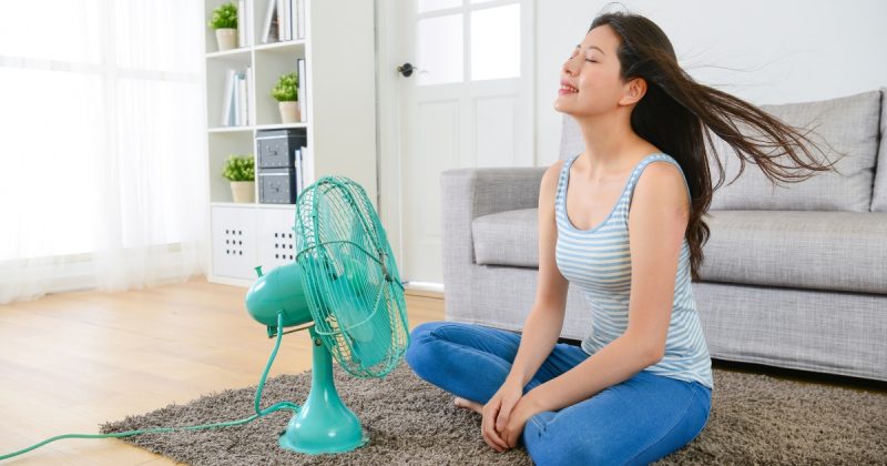 Ventilador ligado em direção à mulher sentada no chão