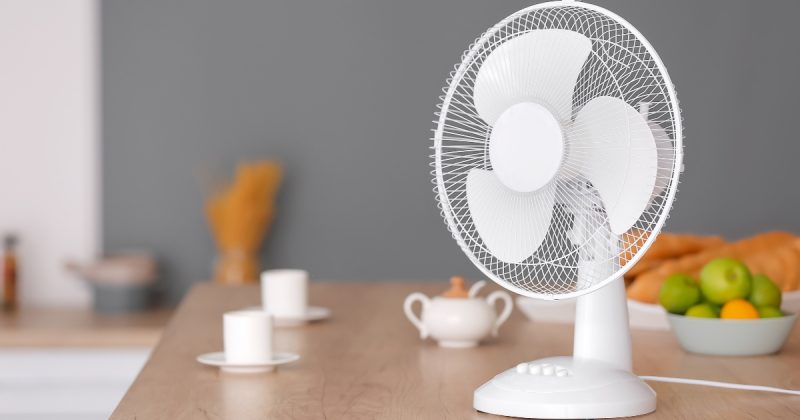 Ventilador branco em cima de mesa com xícaras