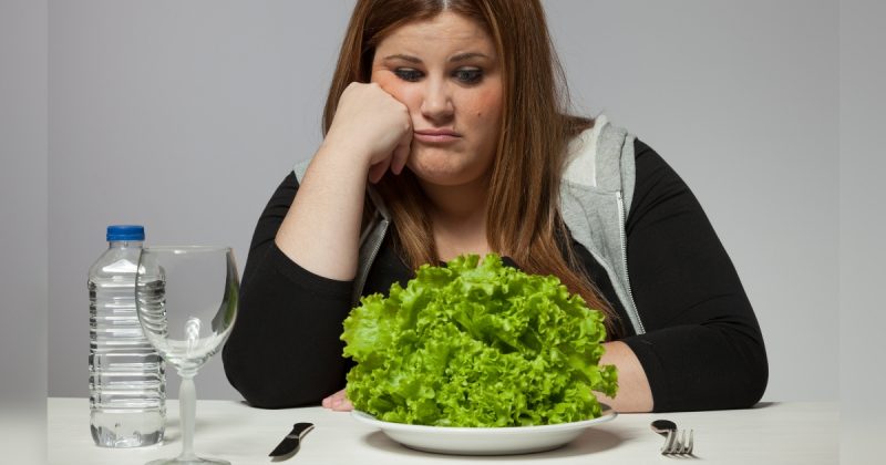 Mulher triste olhando para prato de salada