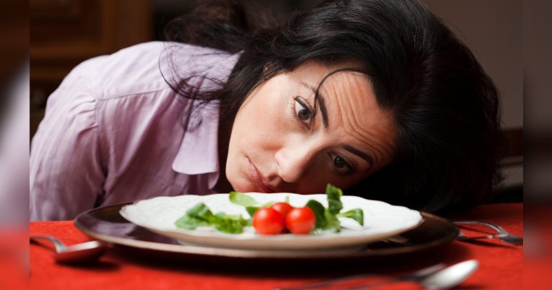 Mulher deitada em mesa e olhando para prato com tomates pequenos 