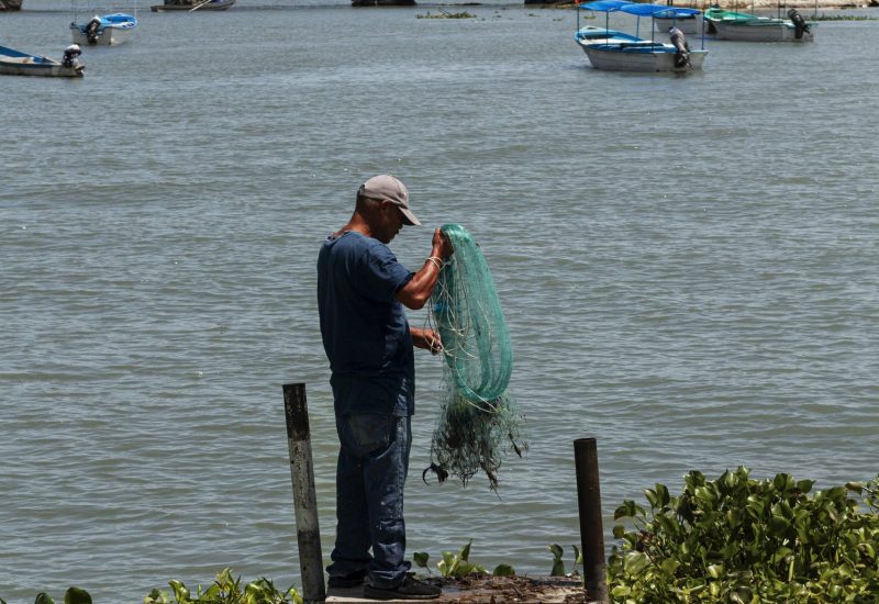 Foto ilustrativa ostra pescador segurando rede com o mar ao fundo