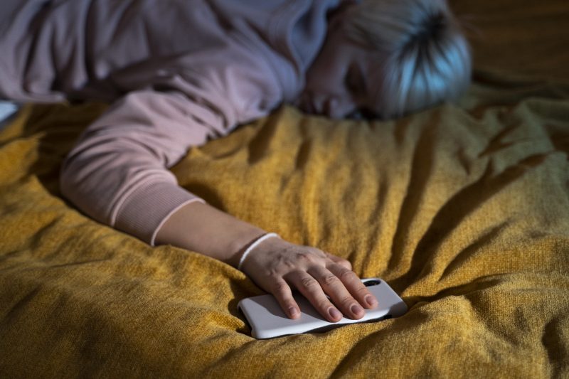 mulher loira dormindo e segurando o celular na cama 