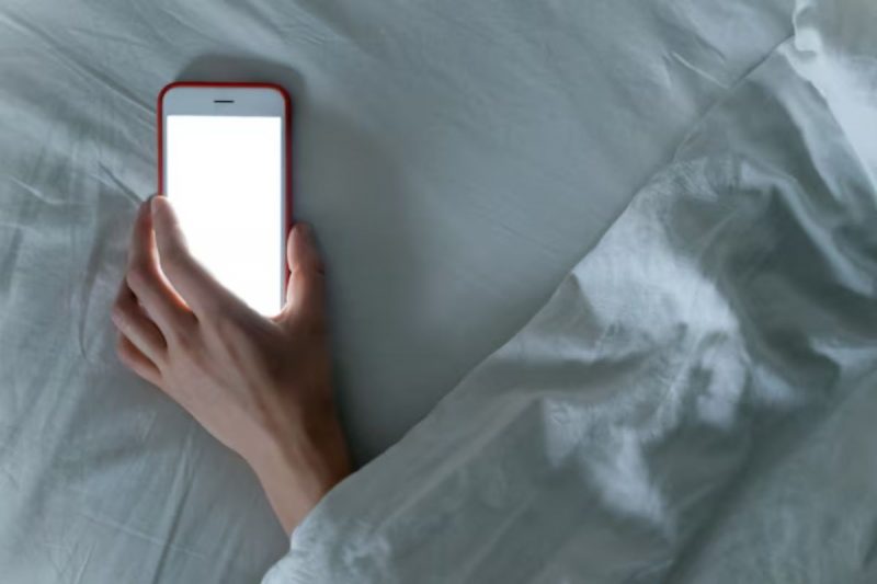 mão segurando um celular na cama enquanto a pessoa dorme 