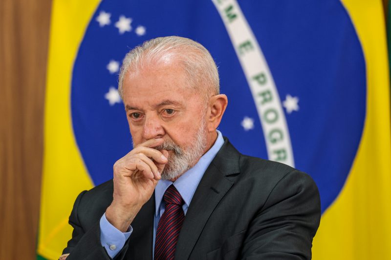 Lula comenta fala de Trump sobre Faixa de Gaza, foto mostra Lula sério com mão na boca em frente à bandeira do Brasil