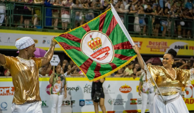 mestre-sala e porta-bandeira na passarela com o pavilhão da escola de samba Os Protegidos da Princesa