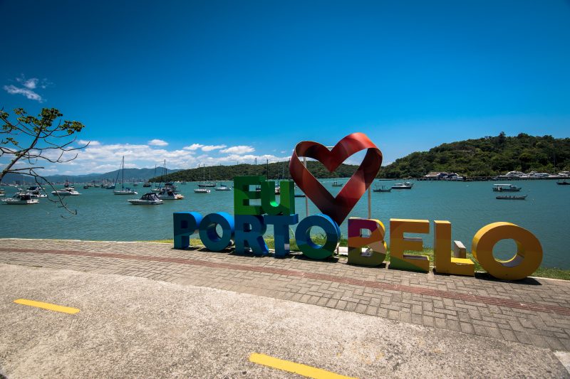 Imagem mostra letreiro do Município de Porto Belo e mar atrás