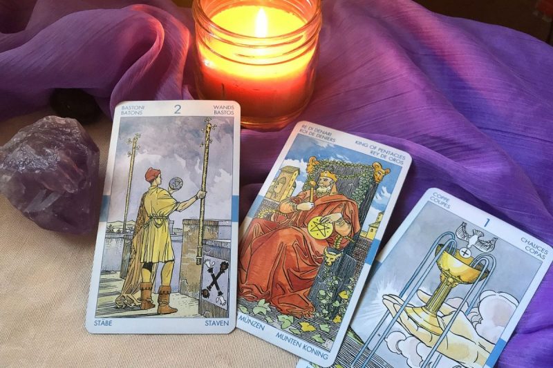 baralho de tarot em cima da mesa com uma vela acesa e um pano roxo