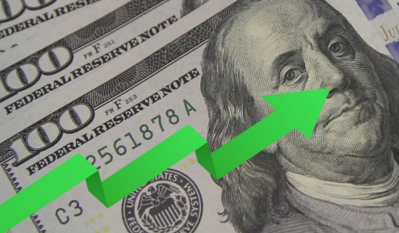 Valor do dólar hoje, foto mostra flecha verde apontando para cima sobre uma cédula de dólar