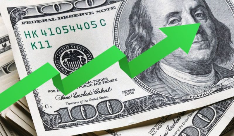 Valor do dólar hoje, foto mostra flecha verde sobre cédula de dólar