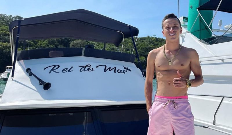 Acidente de jet ski mata ‘rei do mar’ em Itapema, foto mostra homem sem camisa, com bermuda cor de rosa, ao lado de lancha onde está escrita "rei do mar"