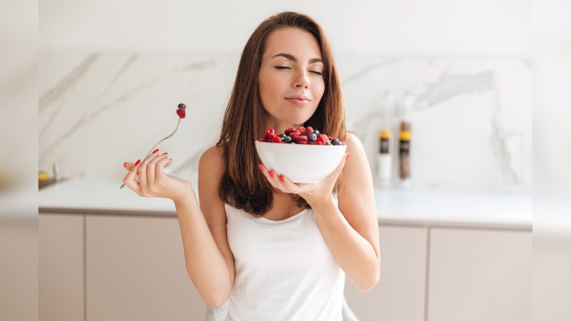 Mulher comendo ameixa e amoras com os olhos fechados