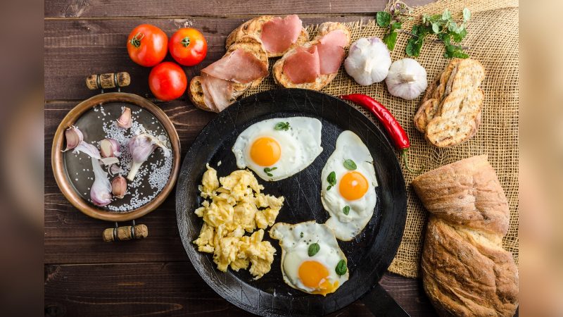 Imagem ovos, tomates, carnes, alhos, pão, dentro de panela e por cima de mesa