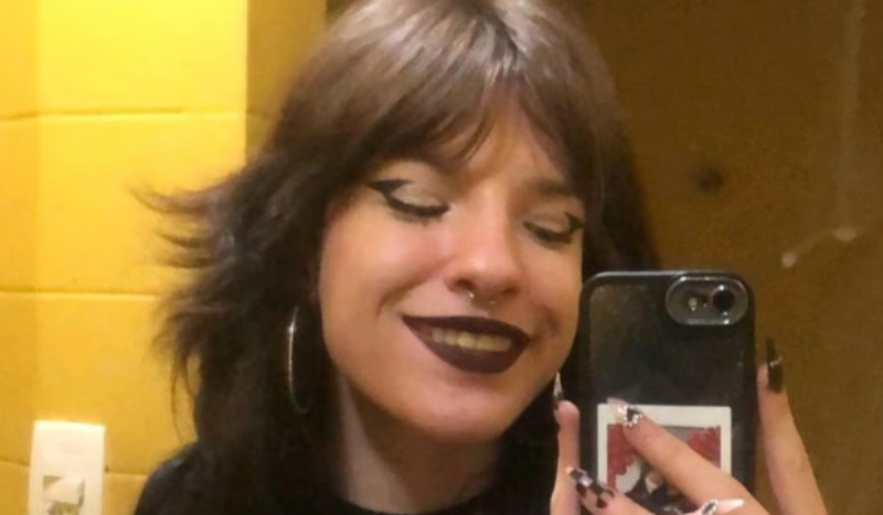 Clara Maria morreu aos 21 anos, foto mostra jovem ruiva, de franja e maquiada tirando foto no espelho, ela sorri