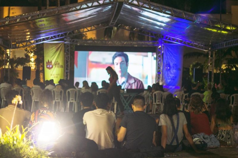 sessões gratuitas de cinema em Joinville ao ar livre. Pessoas sentadas assistindo um filme em uma praça