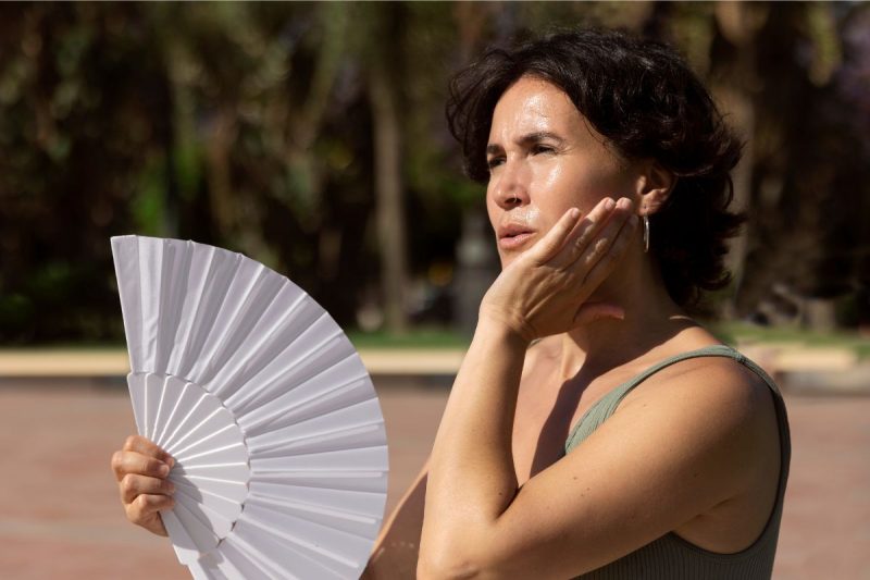 mulher com calor segurando um leque para abanar 