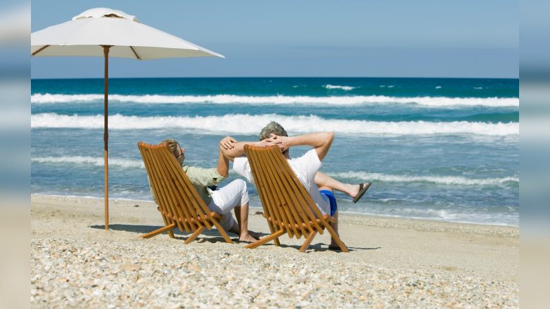Imagem de dois idosos sentados em cadeira de madeira na praia