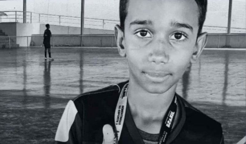 Menino morre após ser atacado por cães, foto mostra menino negro olhando para foto e fazendo um "jóia" com a mão