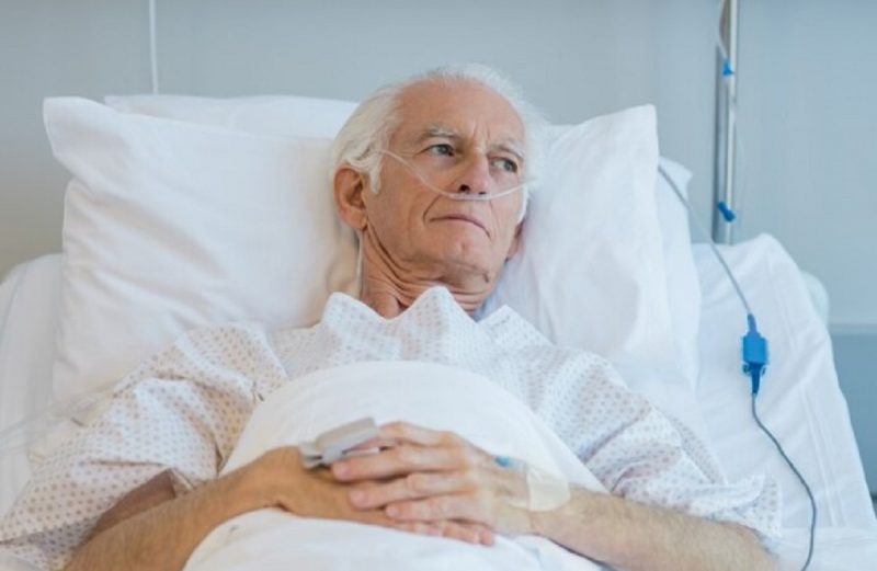 na foto aparece um homem com câncer na cama esperando o médico