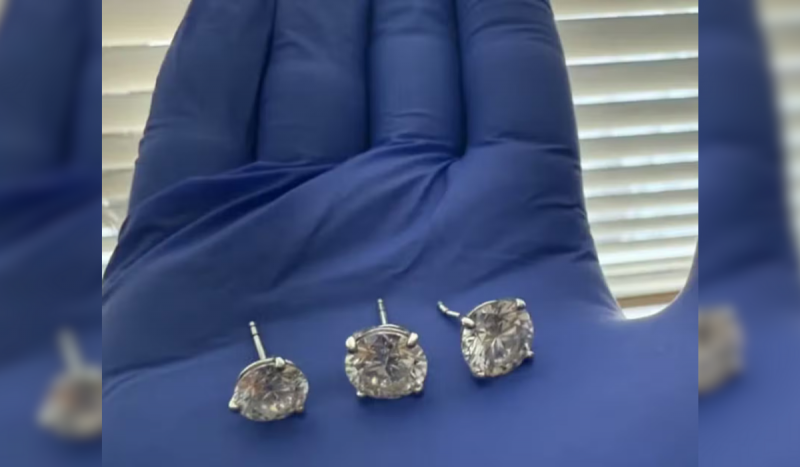 Mão com luva azul segurando três brincos de diamantes