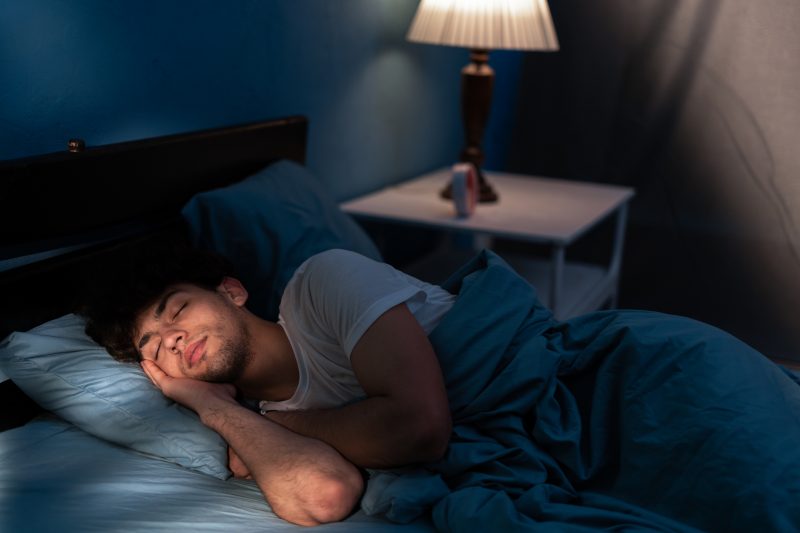 Jovem tranquilo dormindo em uma cama confortável sozinho em casa, desfrutando de seu colchão ortopédico e travesseiro aconchegante